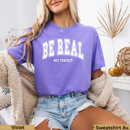 Purple t-shirt with "BE REAL NOT PERFECT" text, worn by a woman.