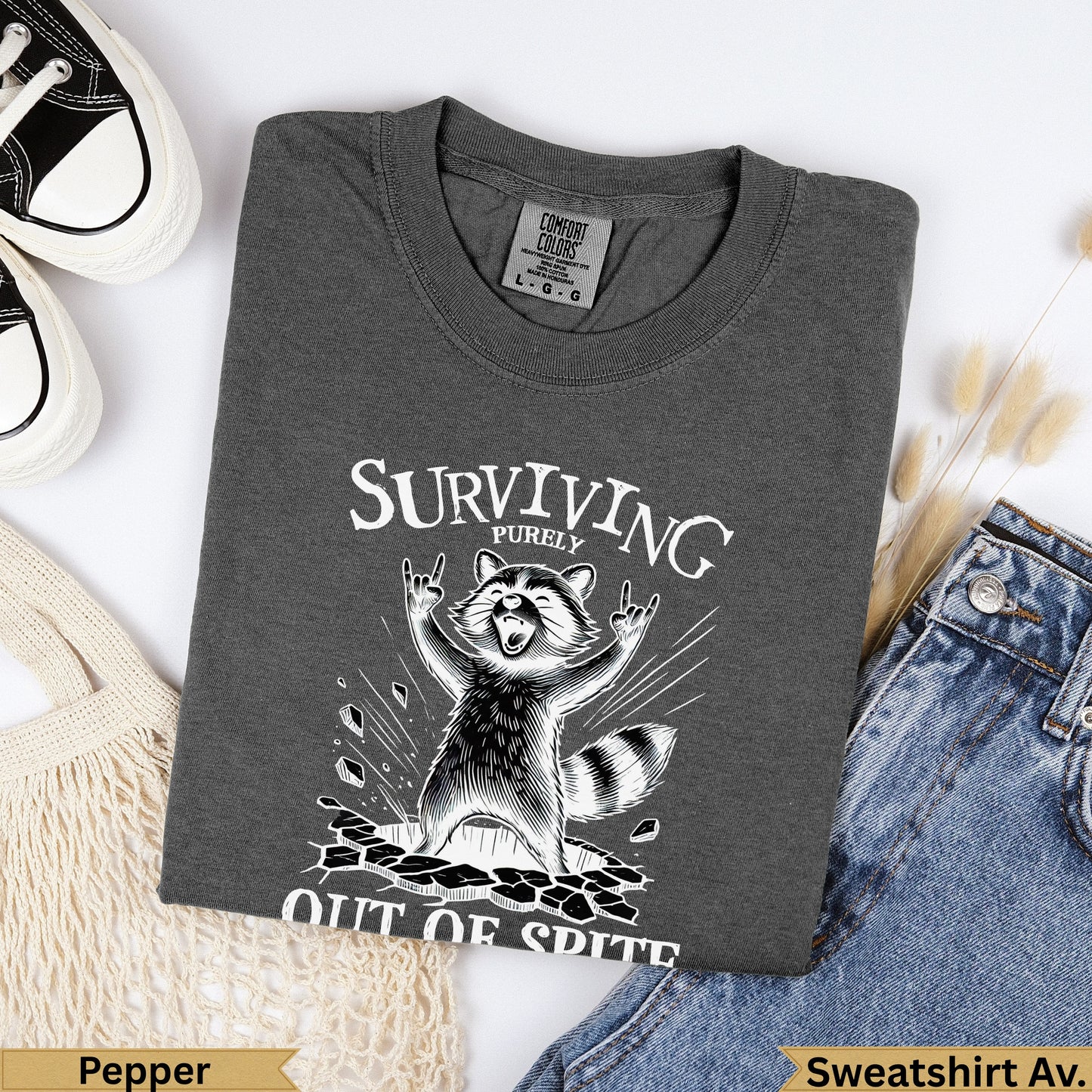 Dark gray Comfort Colors t-shirt with a distressed raccoon graphic saying "Surviving Purely Out of Spite".