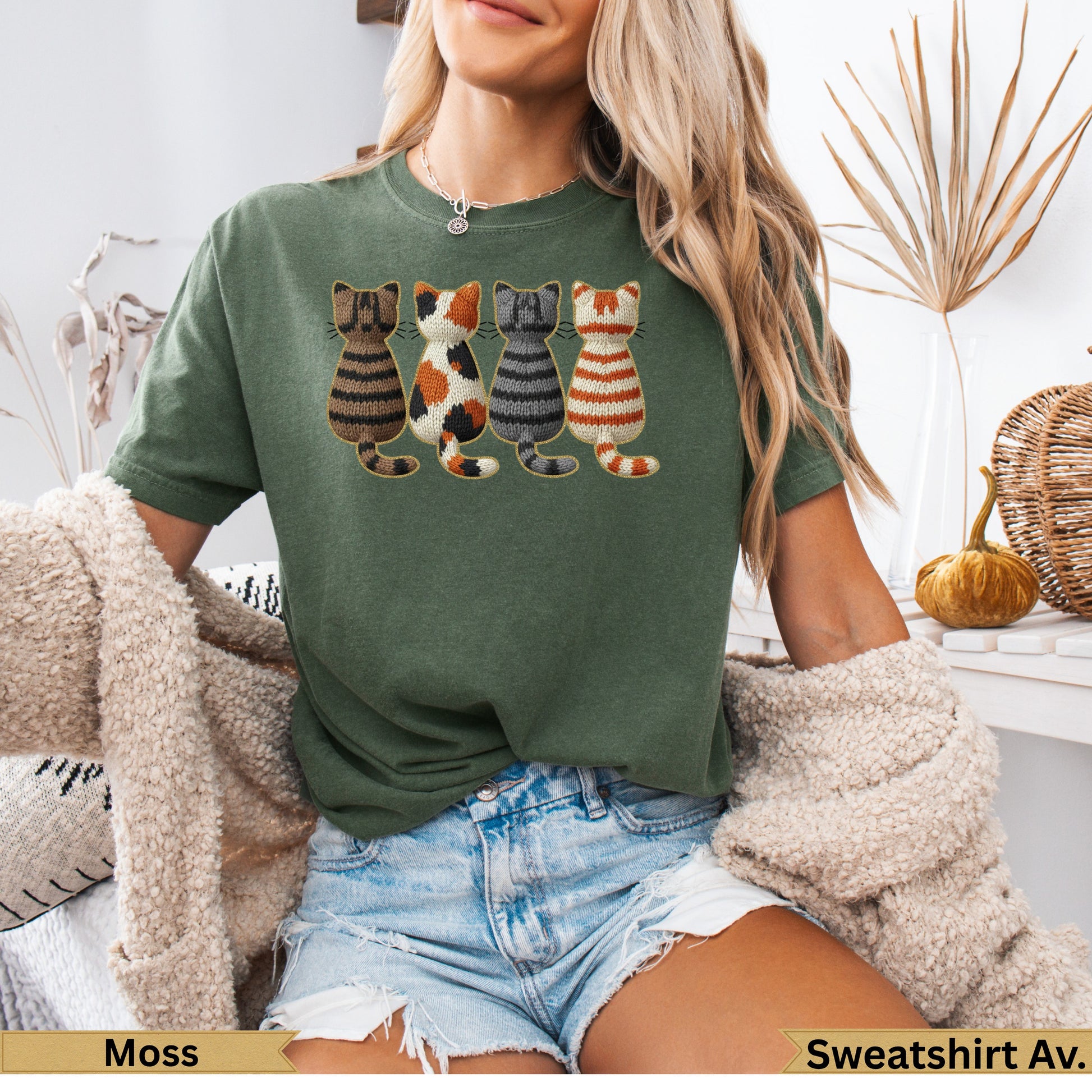 Green t-shirt with four knit-style cats in a row on the chest.