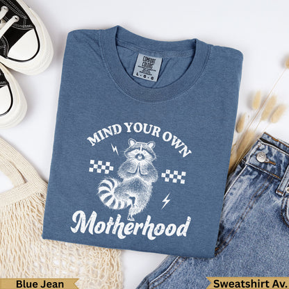 Blue Jean sweatshirt with "Mind Your Own Motherhood" and raccoon graphic.