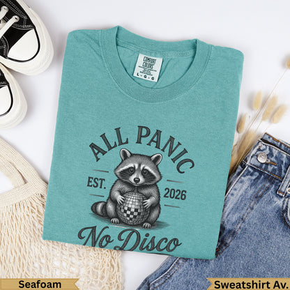 Teal t-shirt with raccoon holding disco ball, "All Panic Est. 2026 No Disco" text.