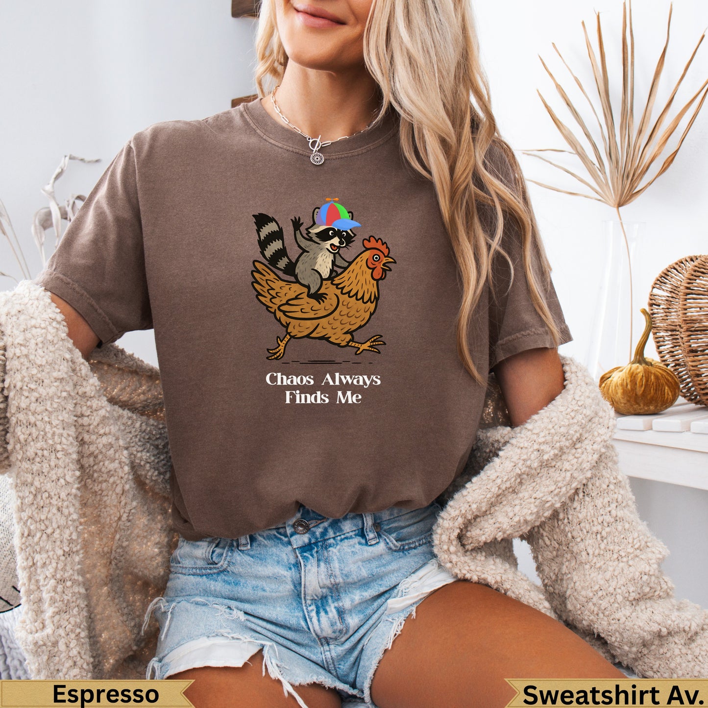 Brown t-shirt with raccoon on chicken, text "Chaos Always Finds Me".