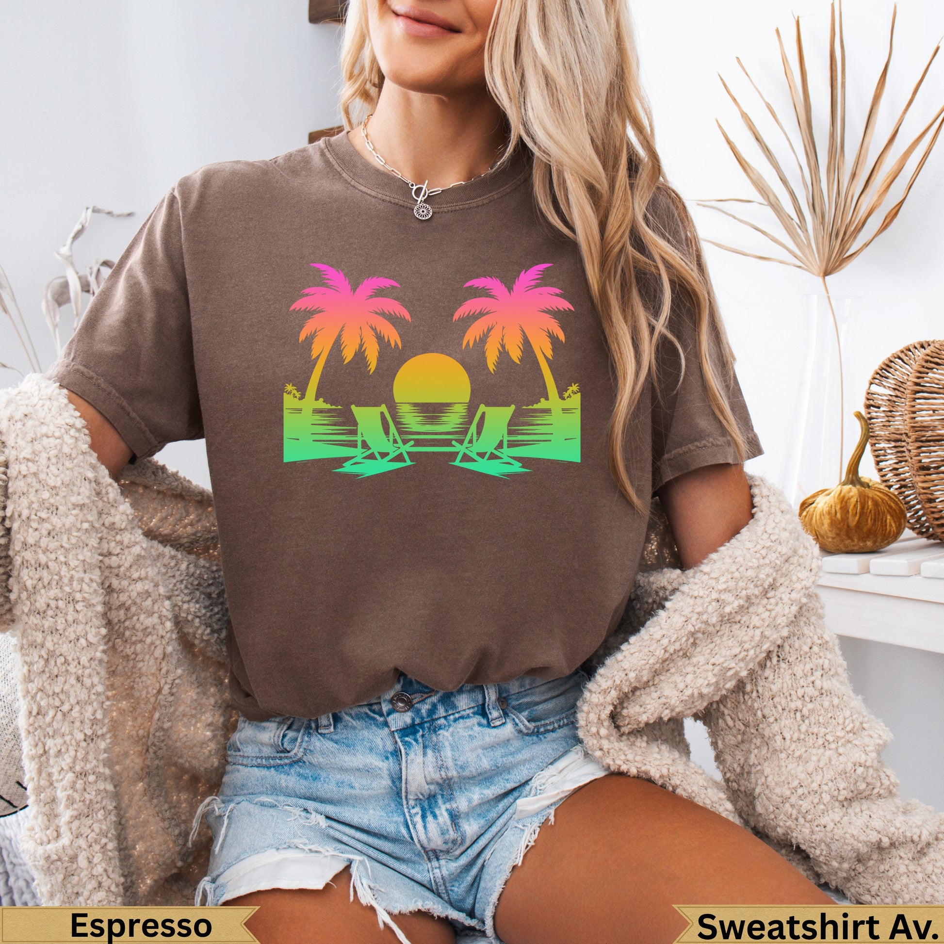 T-shirt graphic with two palm trees, beach chairs, and sunset over water.