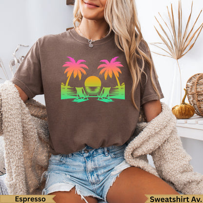 T-shirt graphic with two palm trees, beach chairs, and sunset over water.