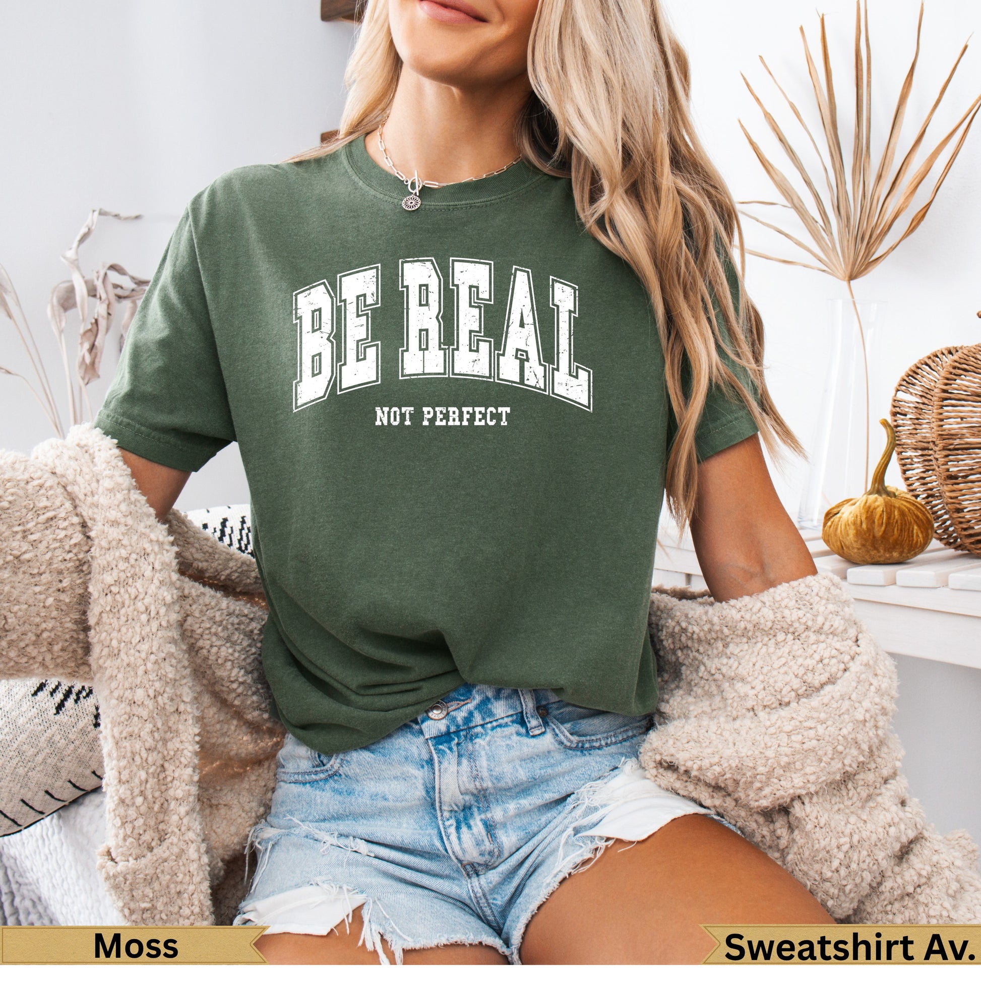 Green t-shirt with "BE REAL NOT PERFECT" text, worn by a woman.