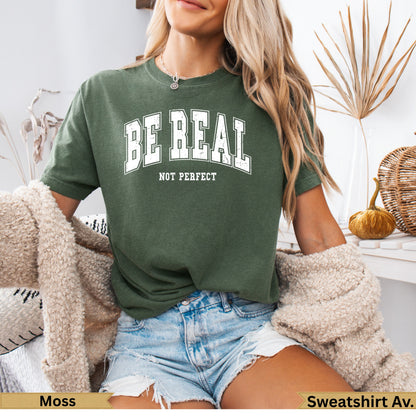 Green t-shirt with "BE REAL NOT PERFECT" text, worn by a woman.