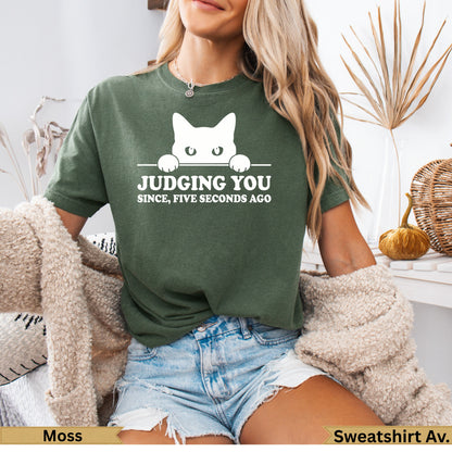Moss green t-shirt with white cat peeking over text "Judging you since five seconds ago."