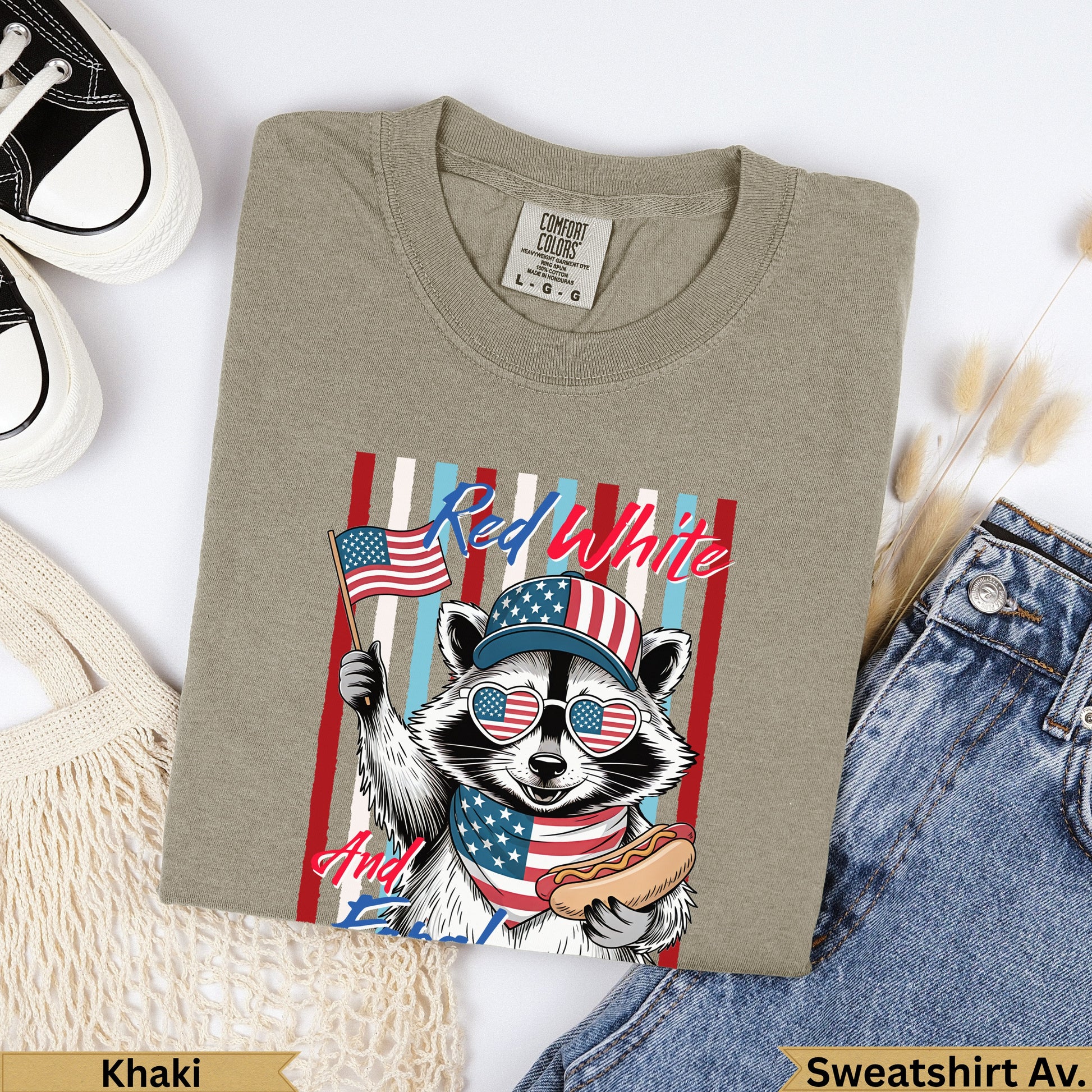 Raccoon wearing a patriotic hat and bandana holding an American flag and hot dog.