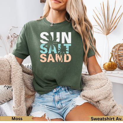 Green t-shirt with "SUN SALT SAND" text, woman wearing it with denim shorts.