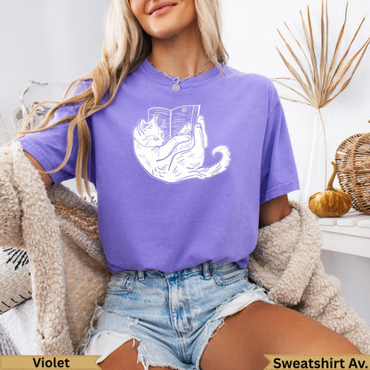 Woman wearing a purple t-shirt with a white cat reading a book graphic.