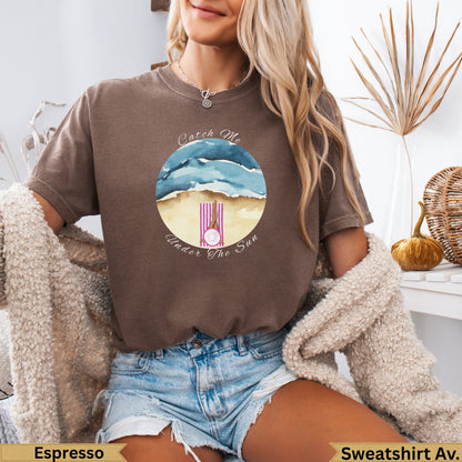 Brown t-shirt with watercolor beach scene and "Catch Me Under The Sun" text.