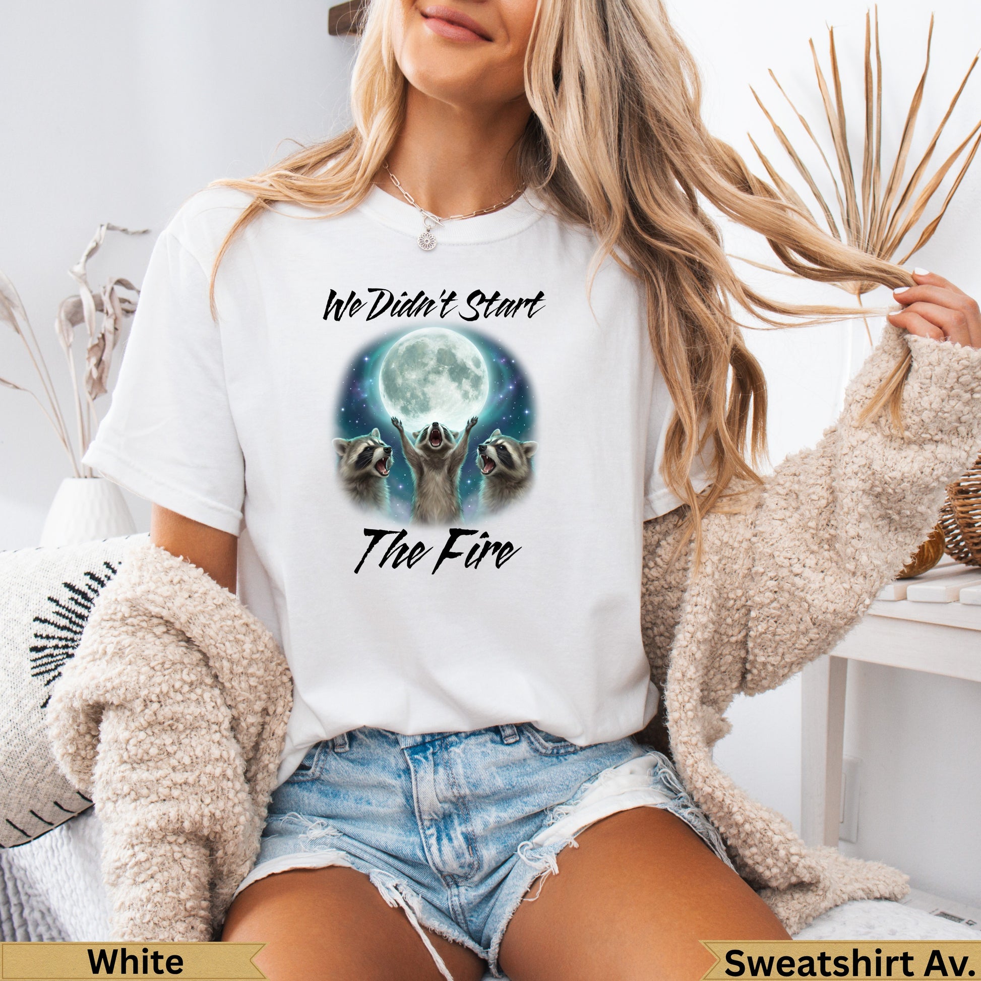 White crewneck sweatshirt with raccoons looking at a full moon and "We didn't start the fire" text.