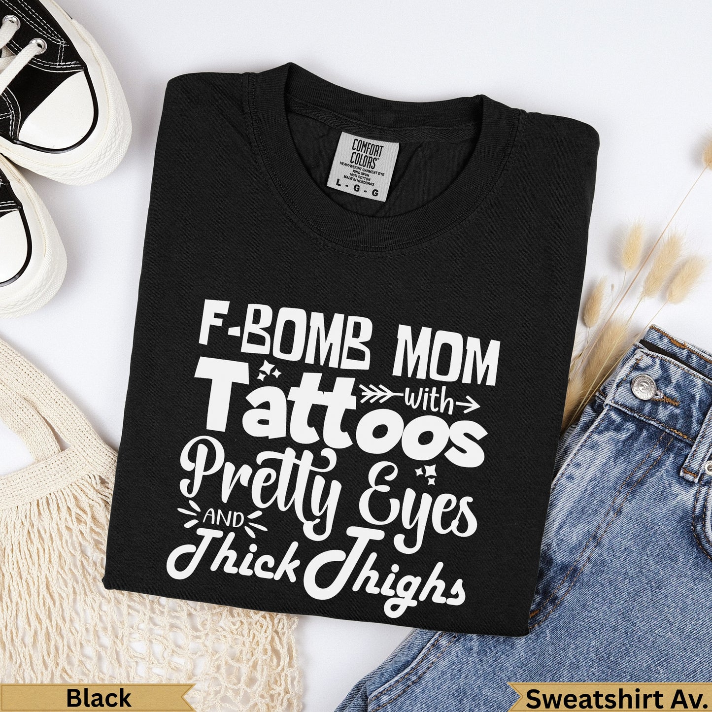 Black Comfort Colors sweatshirt with "F-bomb Mom with Tattoos, Pretty Eyes, and Thick Thighs" text.