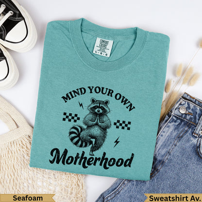 Teal sweatshirt with raccoon and "Mind Your Own Motherhood" text.