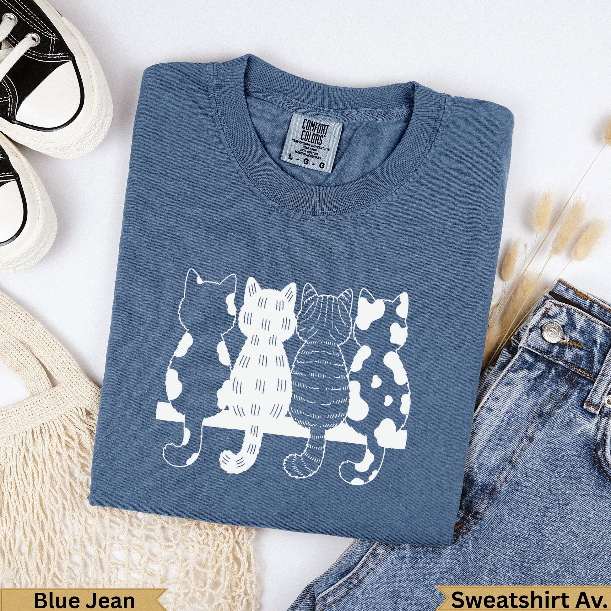 Blue t-shirt with four stylized white cats sitting on a bench.