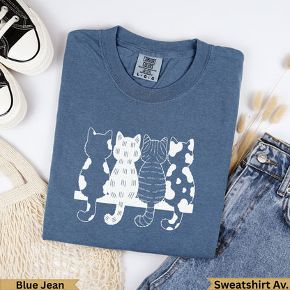 Blue t-shirt with four stylized white cats sitting on a bench.