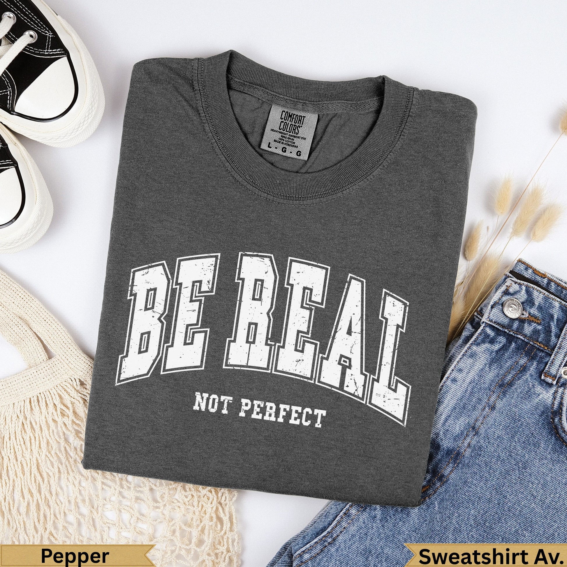 Dark gray t-shirt with "BE REAL NOT PERFECT" text, beside jeans.