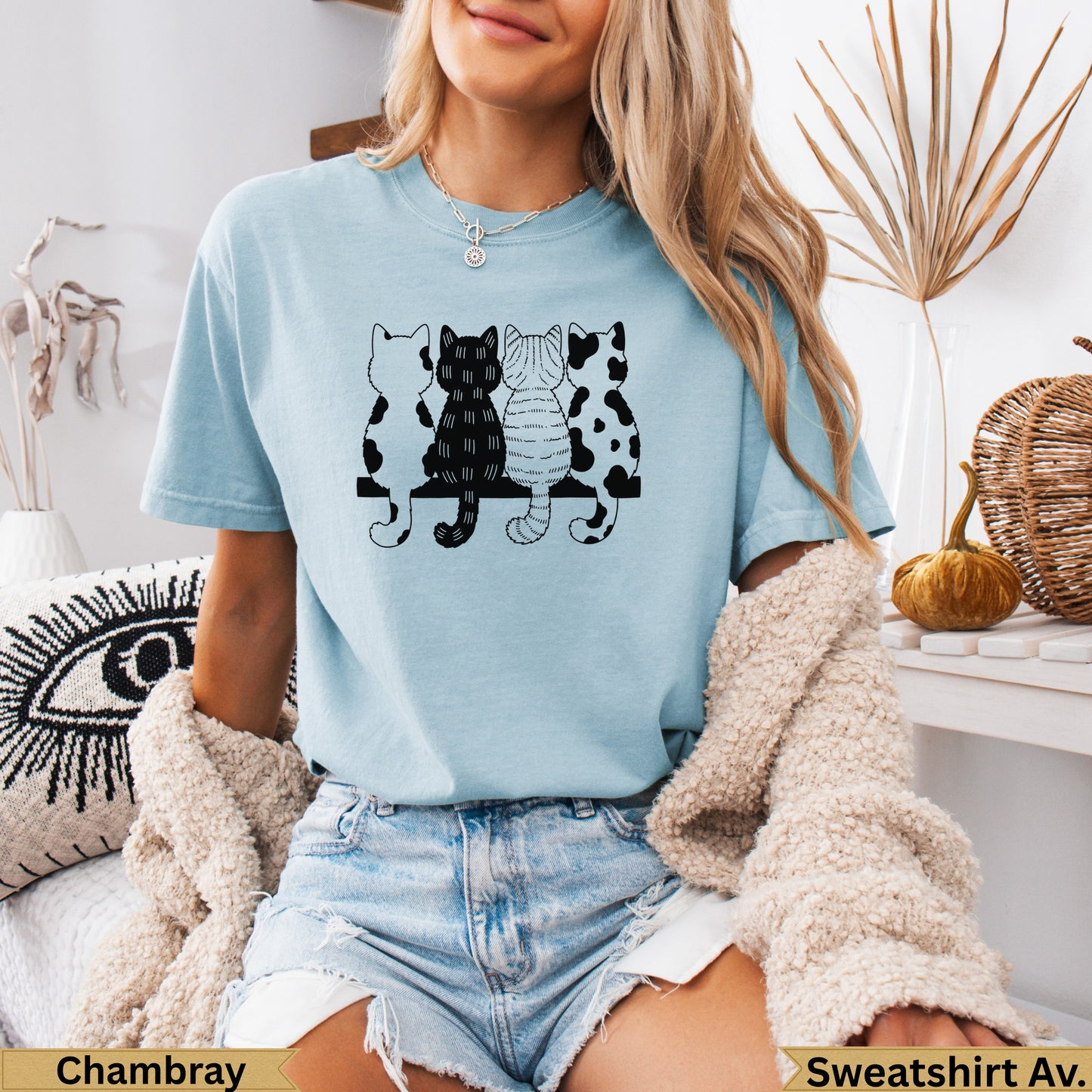 Light blue t-shirt with four cartoon cats sitting on a bench.