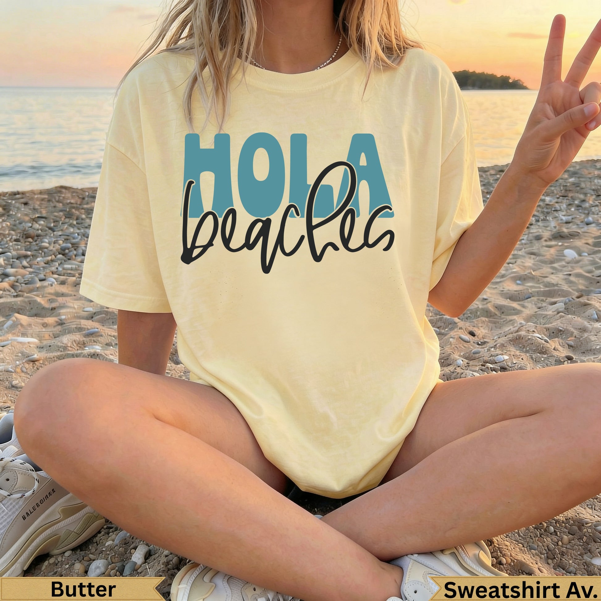 Yellow "Hola beaches" graphic t-shirt on a model sitting on sand.