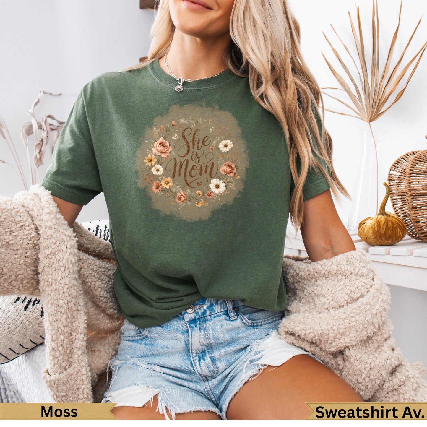 Green t-shirt with "She is Mom" floral graphic on chest.