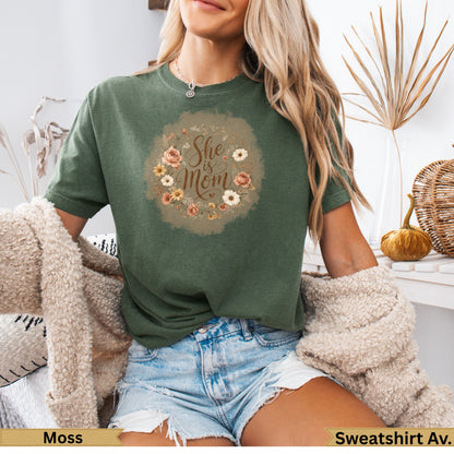 Green t-shirt with "She is Mom" floral graphic on chest.