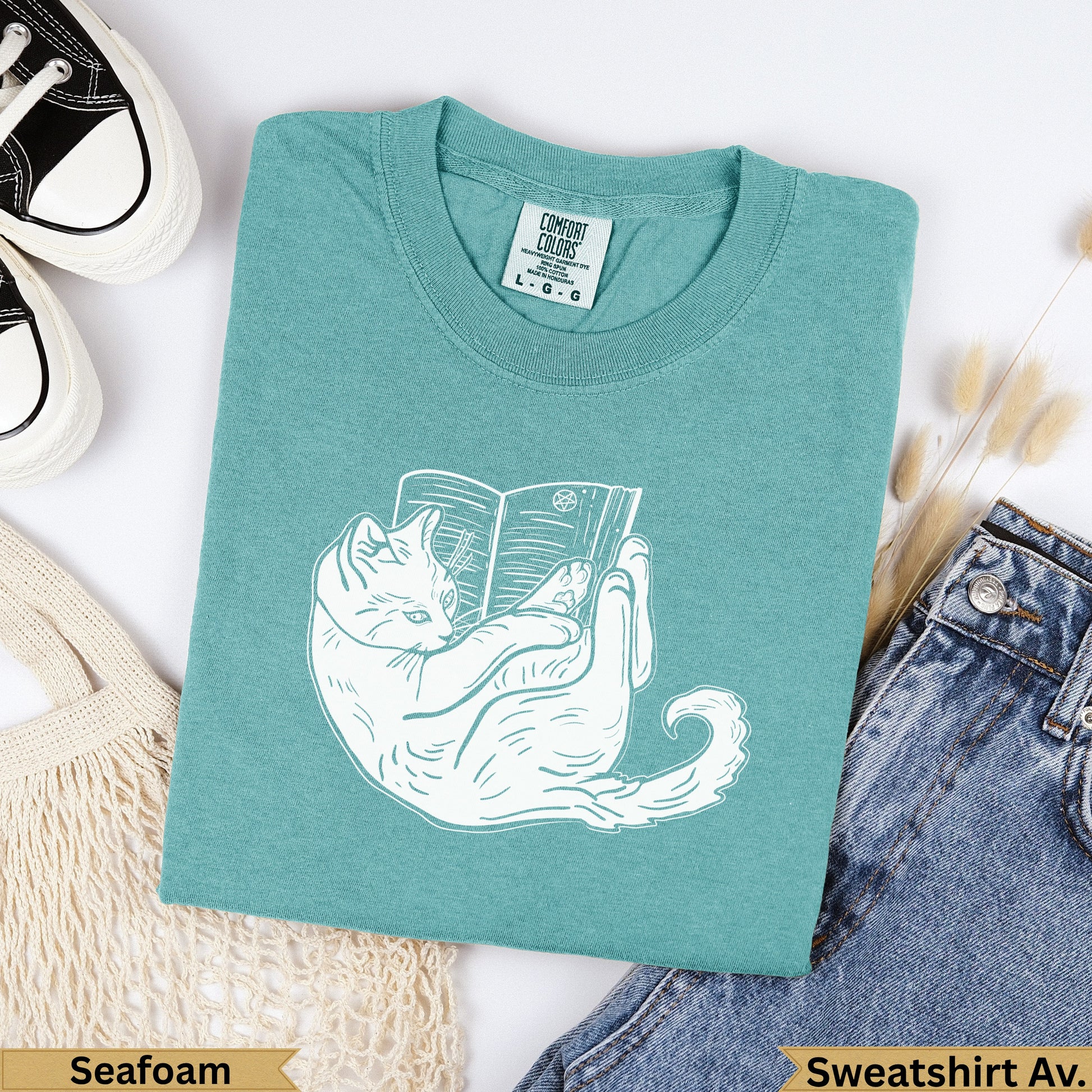 Teal sweatshirt with white cat illustration reading a book, "Seafoam" label.
