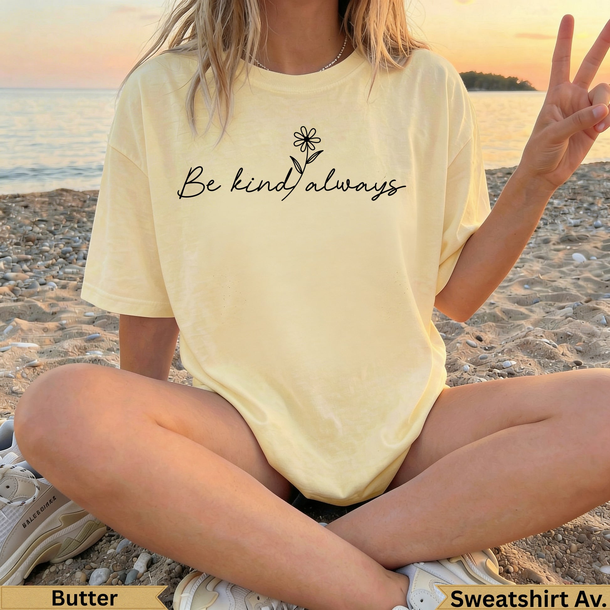 Light yellow "Be Kind Always" t-shirt with daisy graphic, worn by a person on a beach.