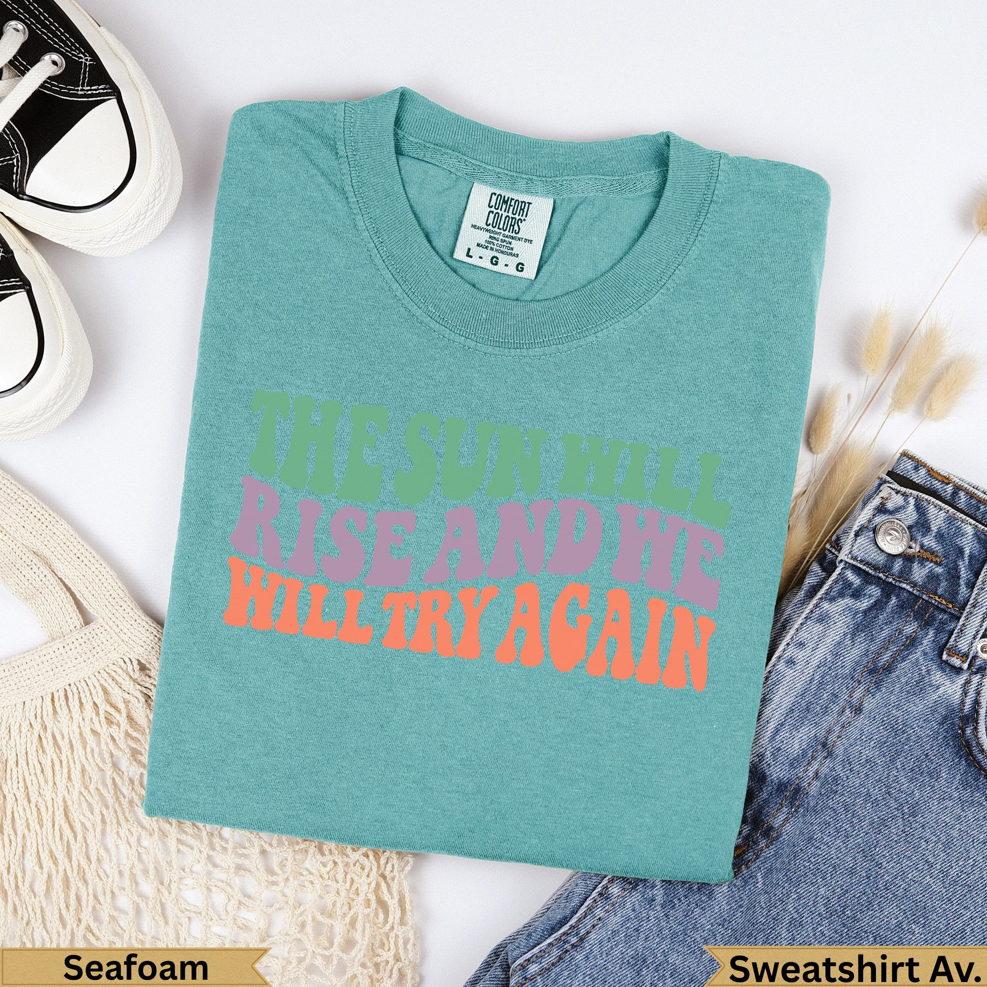 Teal t-shirt with "The sun will rise and we will try again" text.