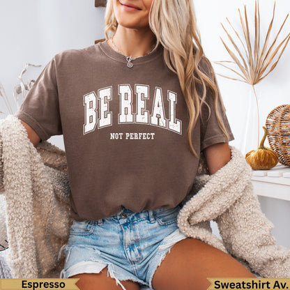 Brown sweatshirt with "BE REAL NOT PERFECT" text, worn by a person.