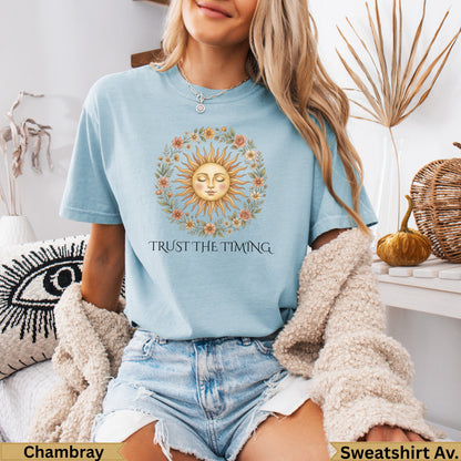 Light blue t-shirt with a sun and floral wreath graphic and text "TRUST THE TIMING".