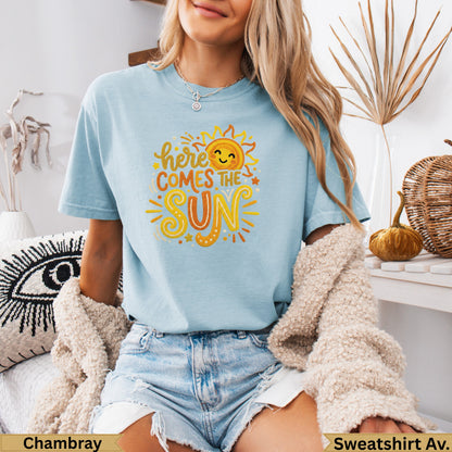 Light blue t-shirt with a smiling sun graphic and "here comes the sun" text.