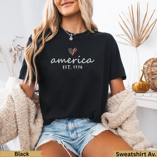 Black crewneck sweatshirt with "America EST. 1776" and heart flag graphic.