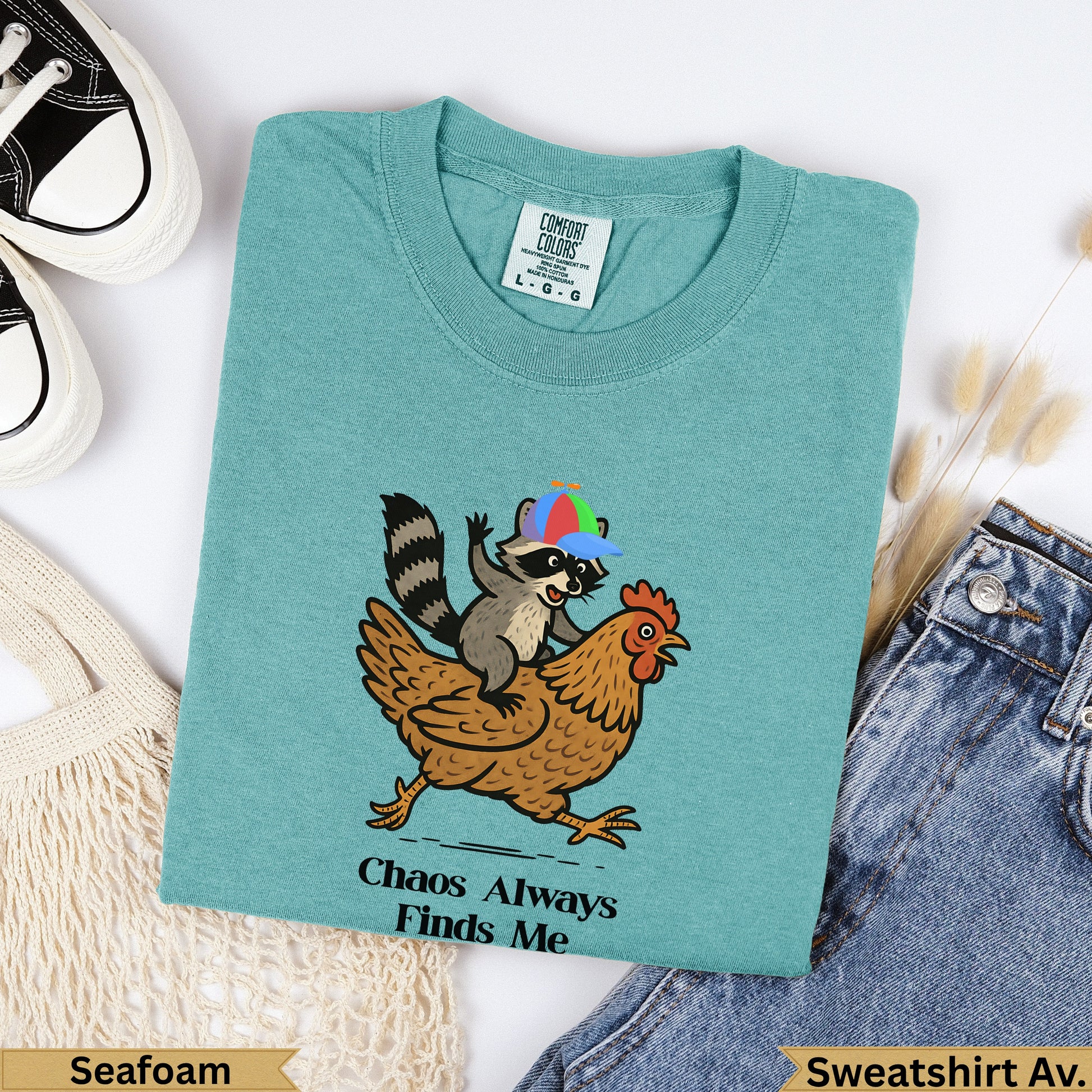 Teal t-shirt with raccoon wearing a hat riding a chicken; "Chaos Always Finds Me" text.
