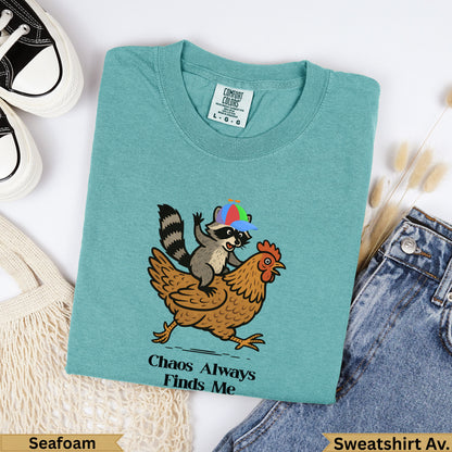Teal t-shirt with raccoon wearing a hat riding a chicken; "Chaos Always Finds Me" text.
