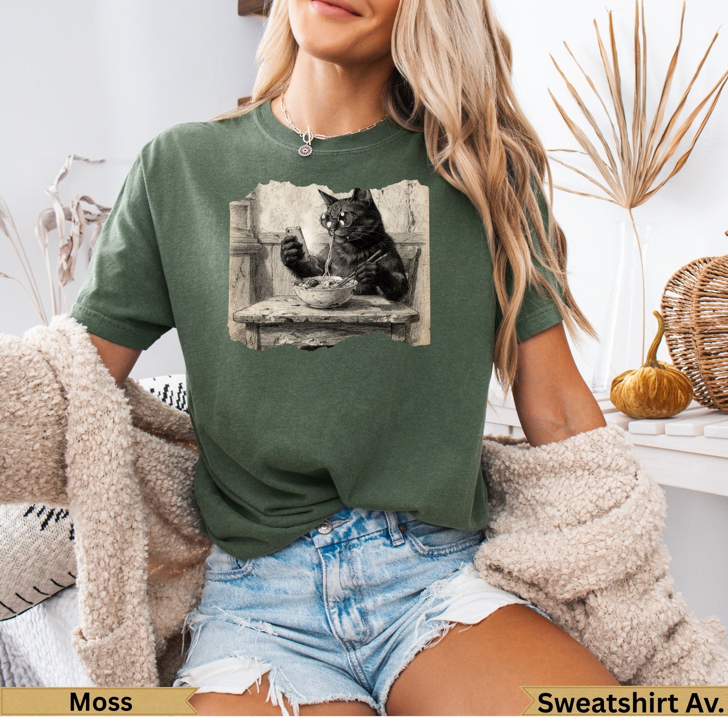 Black cat wearing glasses eats noodles at a table, printed on green t-shirt.
