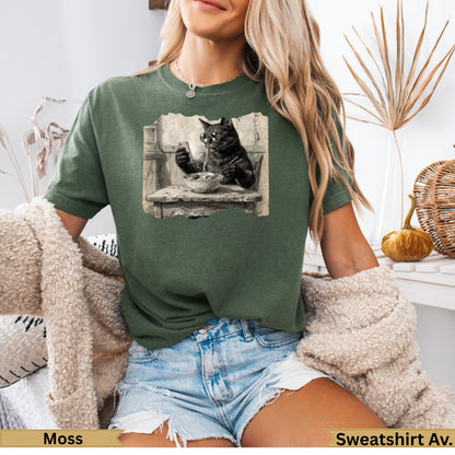 Black cat wearing glasses eats noodles at a table, printed on green t-shirt.
