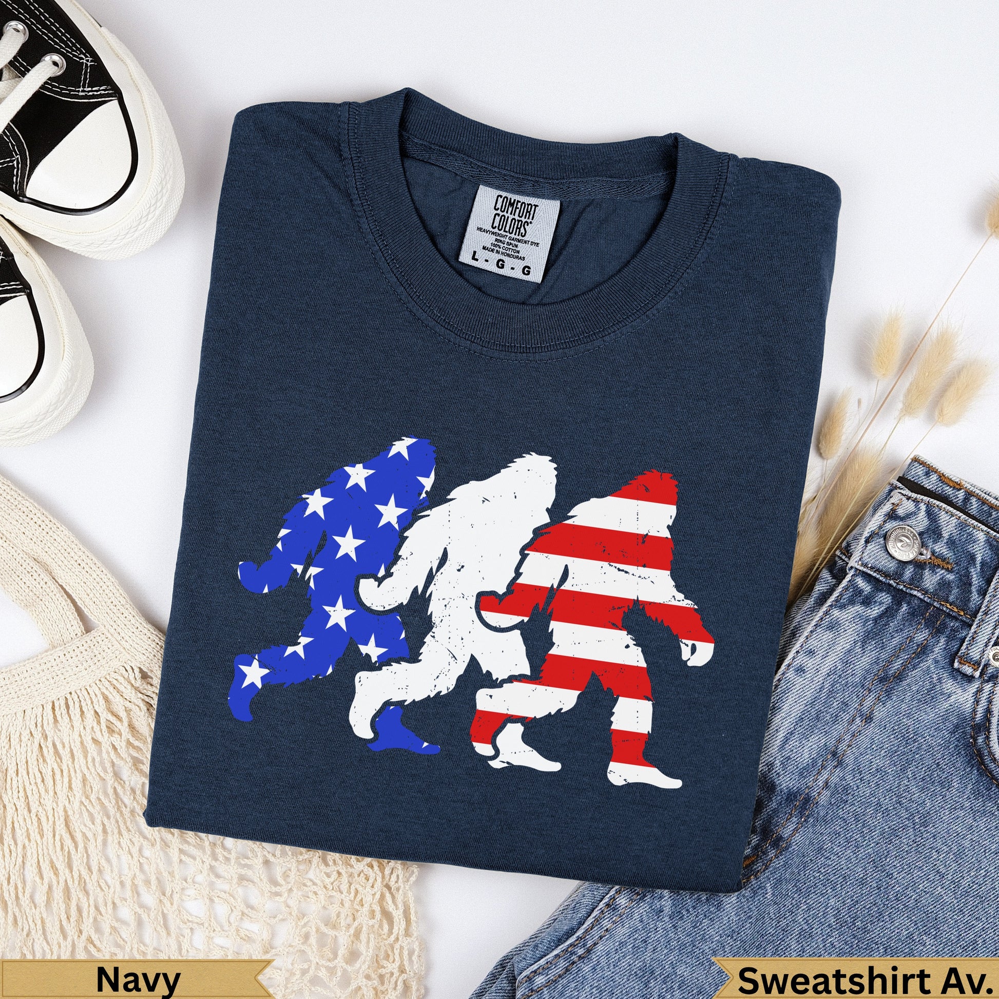 Three Bigfoot silhouettes in patriotic USA flag design on navy t-shirt.