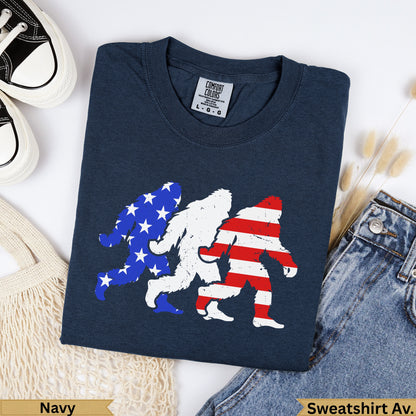 Three Bigfoot silhouettes in patriotic USA flag design on navy t-shirt.