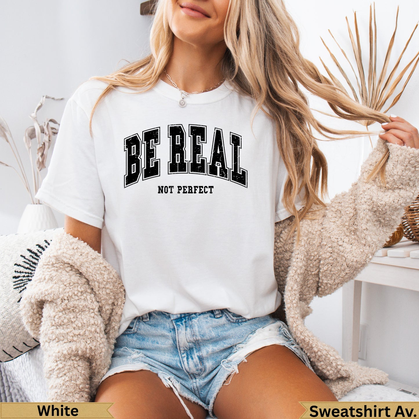 White t-shirt with "BE REAL NOT PERFECT" text, worn by a person.
