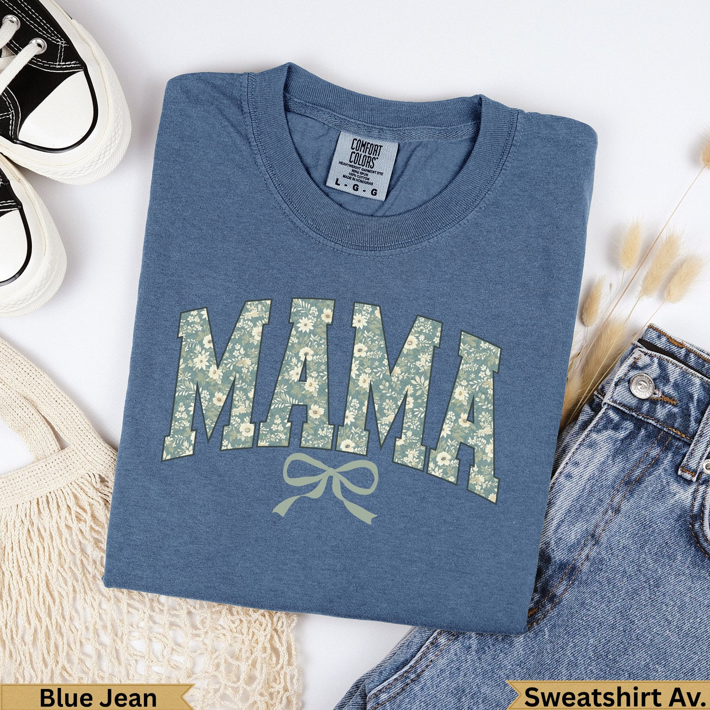 Blue t-shirt with "MAMA" in floral pattern, next to jeans and bag.