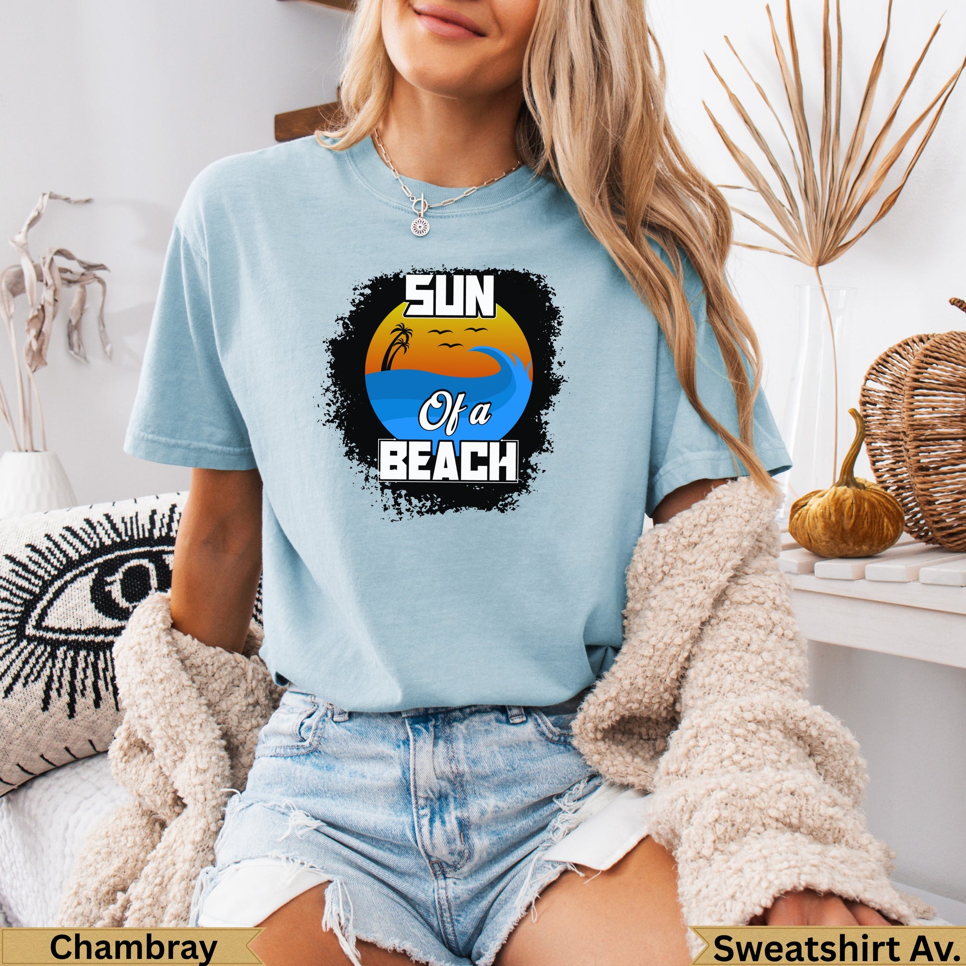 Light blue t-shirt with "Sun of a Beach" text and a sunset over ocean waves graphic.