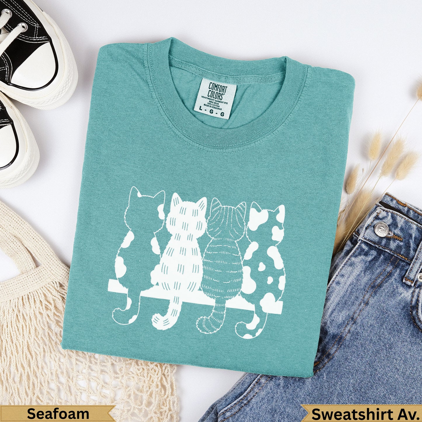 Teal sweatshirt with four white cats lined up on a bench.