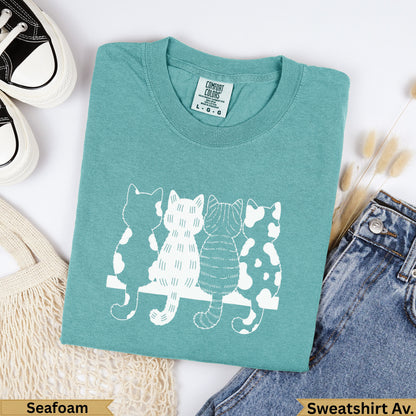 Teal sweatshirt with four white cats lined up on a bench.