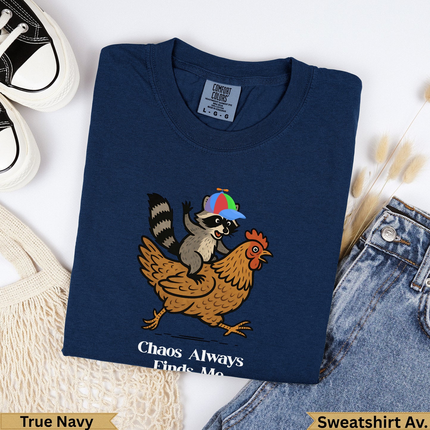 Navy sweatshirt with raccoon riding chicken graphic and "Chaos Always Finds Me" text.