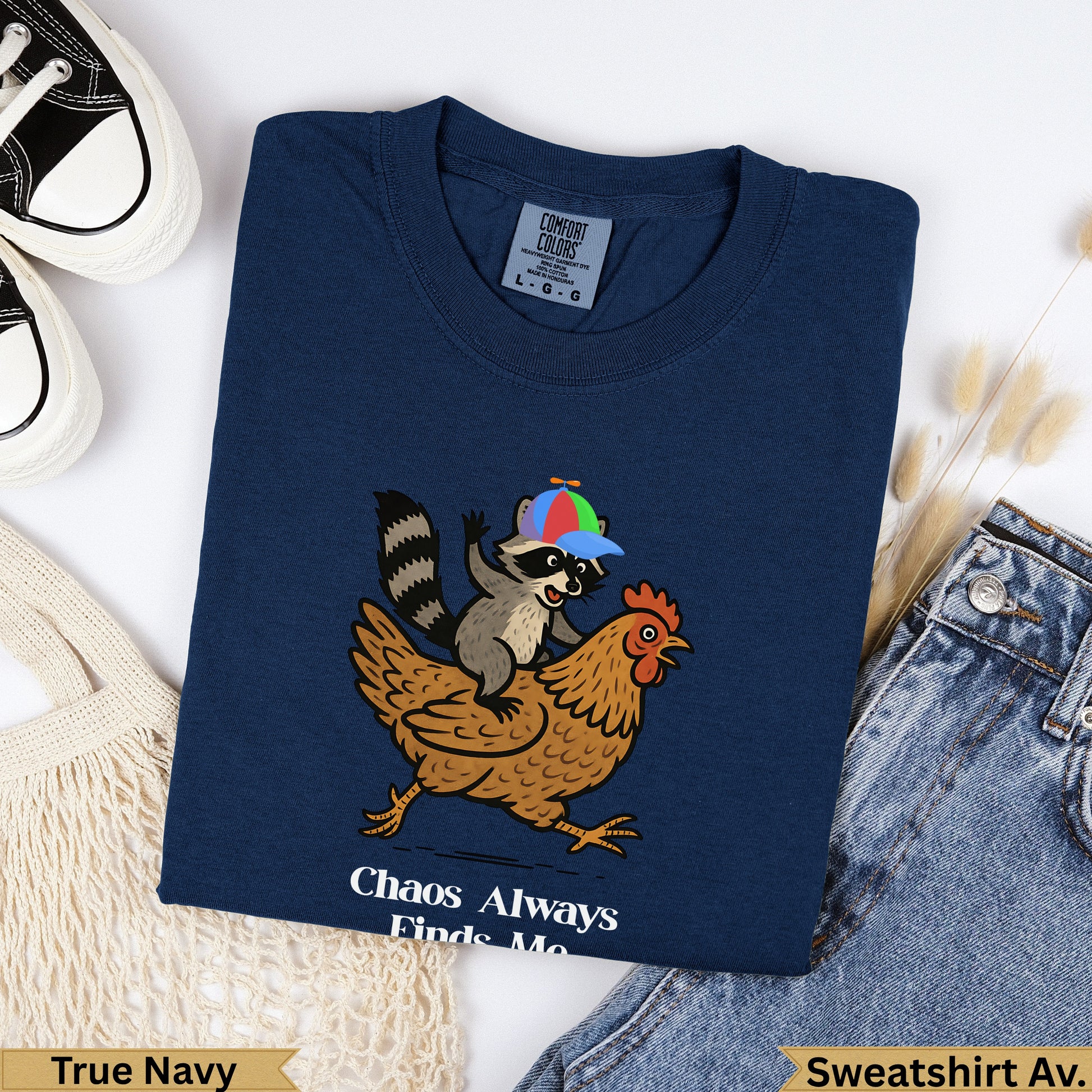 Navy sweatshirt with raccoon riding chicken graphic and "Chaos Always Finds Me" text.