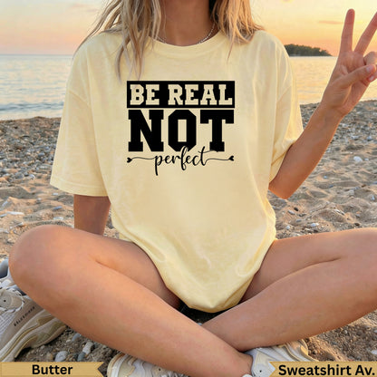 Yellow t-shirt with "BE REAL NOT perfect" text, worn by person on beach.