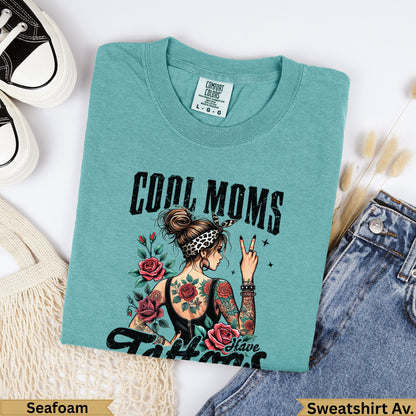 Teal t-shirt with "COOL MOMS" and roses graphic, woman with tattoos.