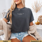 Dark grey t-shirt with "apparently, I am dramatic" text, worn by a woman.