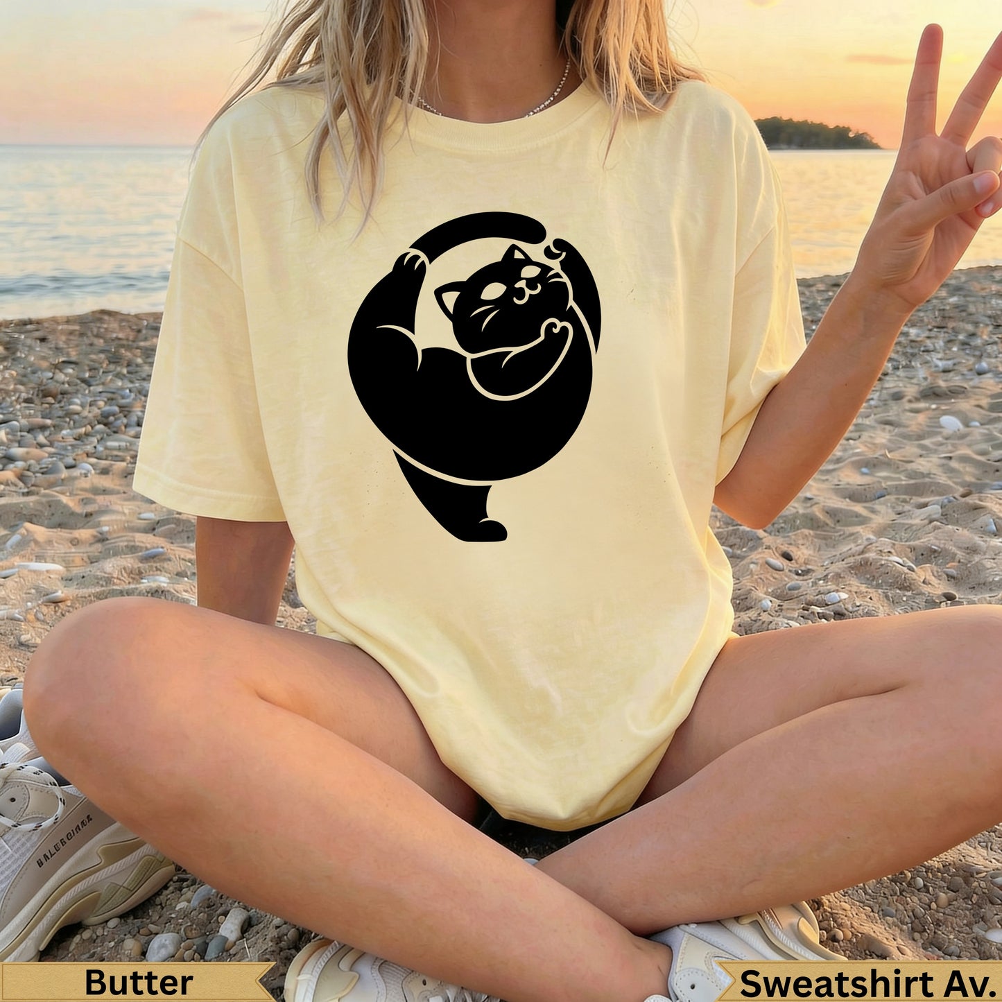 Yellow t-shirt with black cat silhouette design, woman sitting on beach.