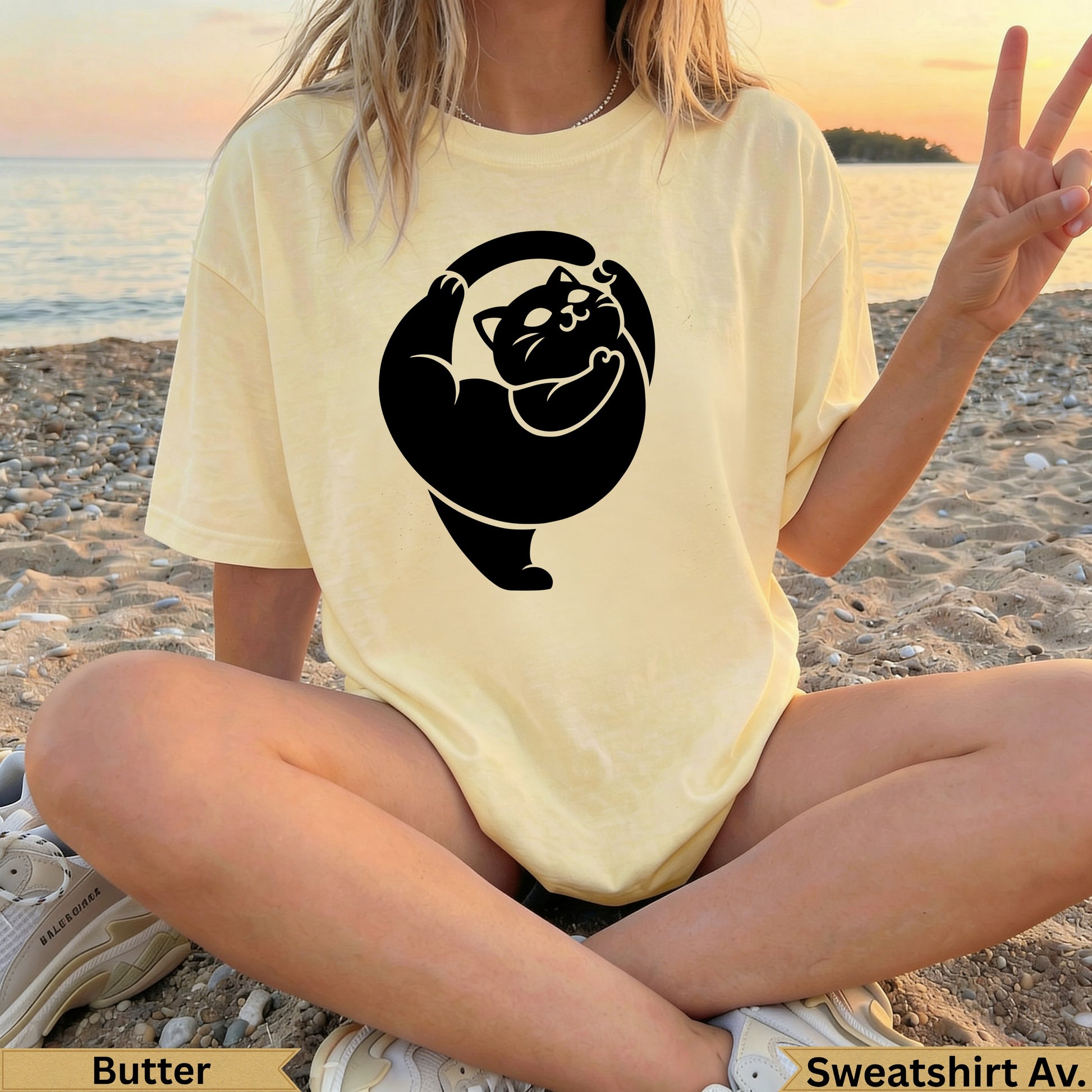 Yellow t-shirt with black cat silhouette design, woman sitting on beach.